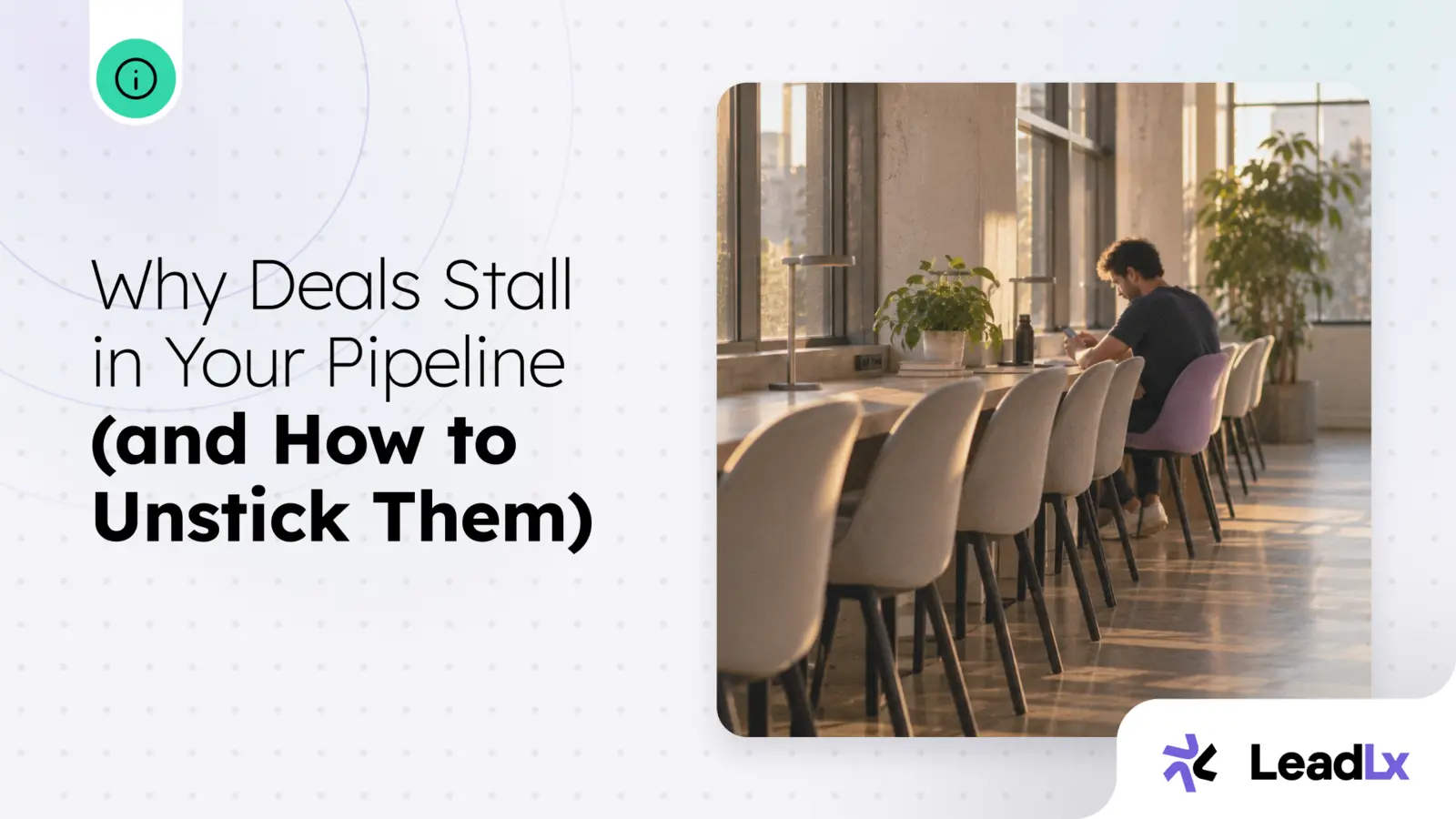A person sitting alone at a long communal table lined with empty chairs, working in a sunlit office
